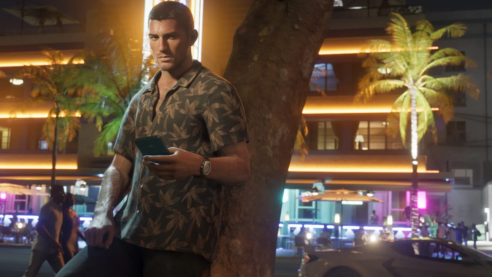 Jason in a patterned shirt leans against a tree on a neon-lit street at night, holding his phone