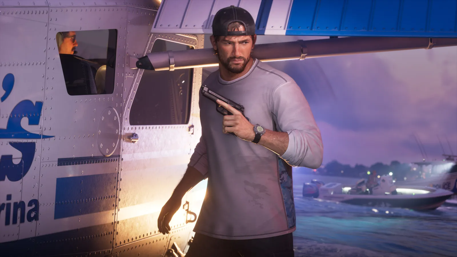 Jason Duval in a backwards cap holds a pistol beside a parked seaplane as a police boat passes behind him