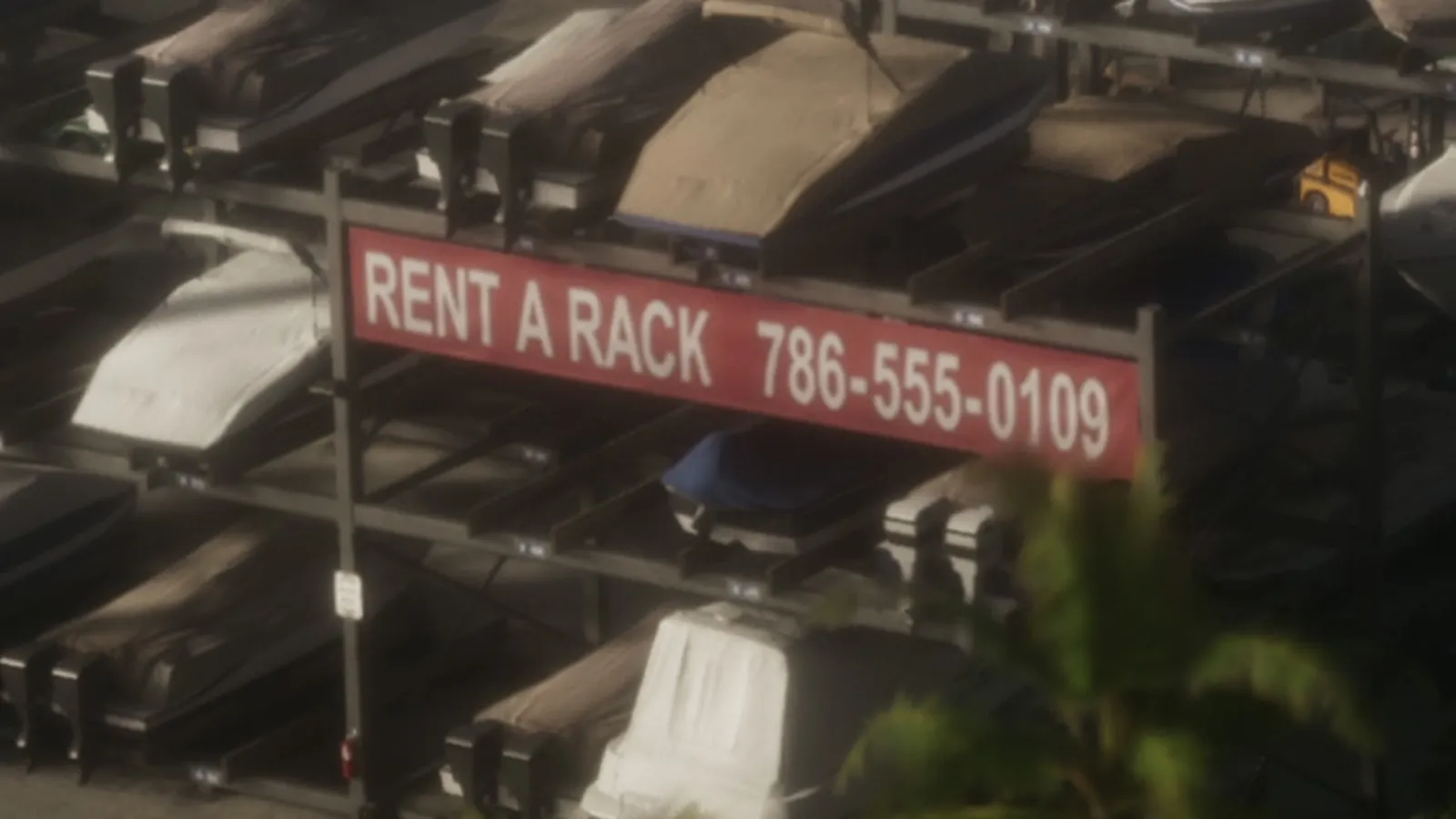 A red Rent a Rack banner with the phone number 786-555-0109 hangs on boat storage racks