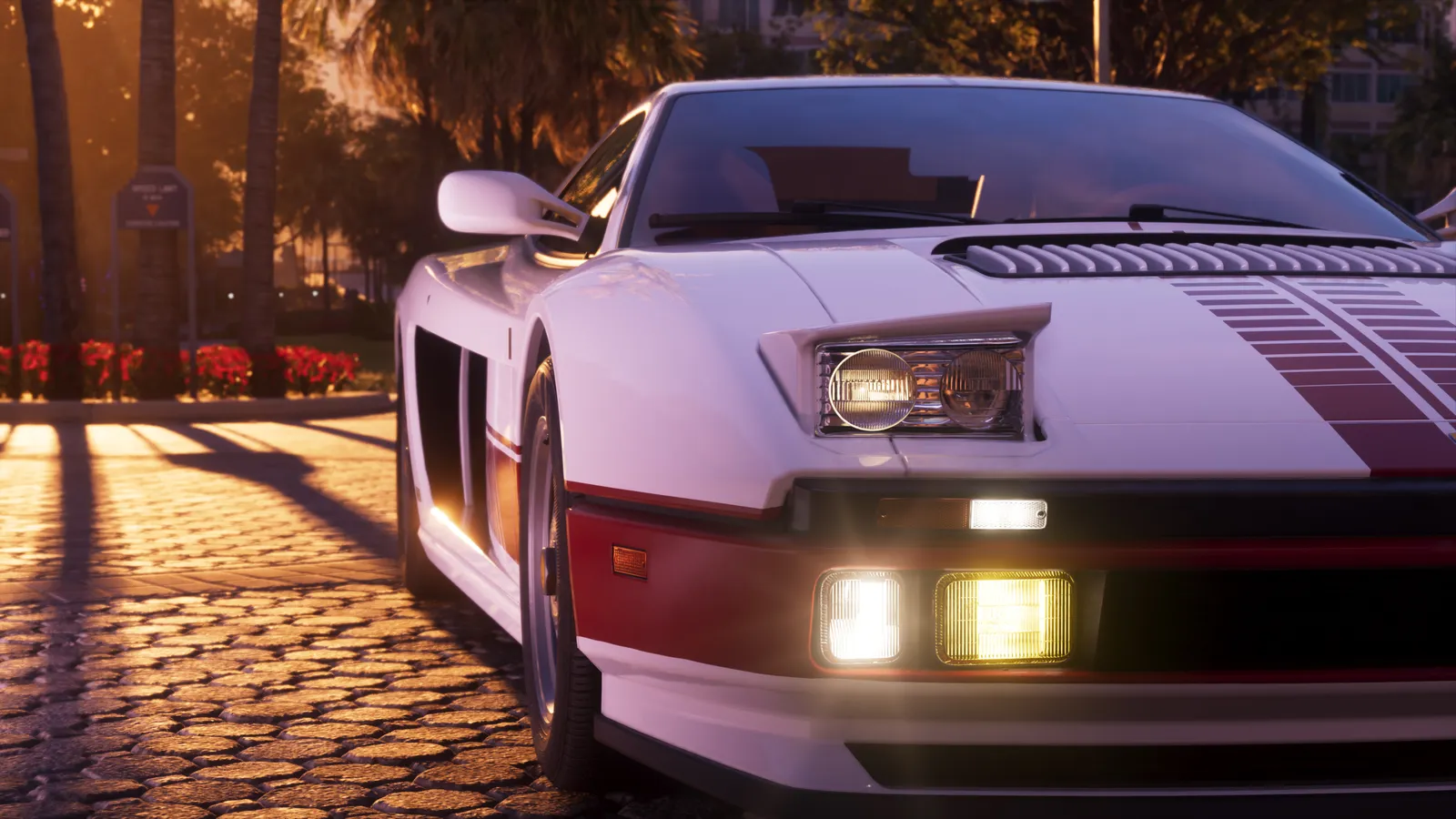 A white Grotti Cheetah with red stripes and its lights on, parked on a cobblestone drive lined with palm trees at sunset
