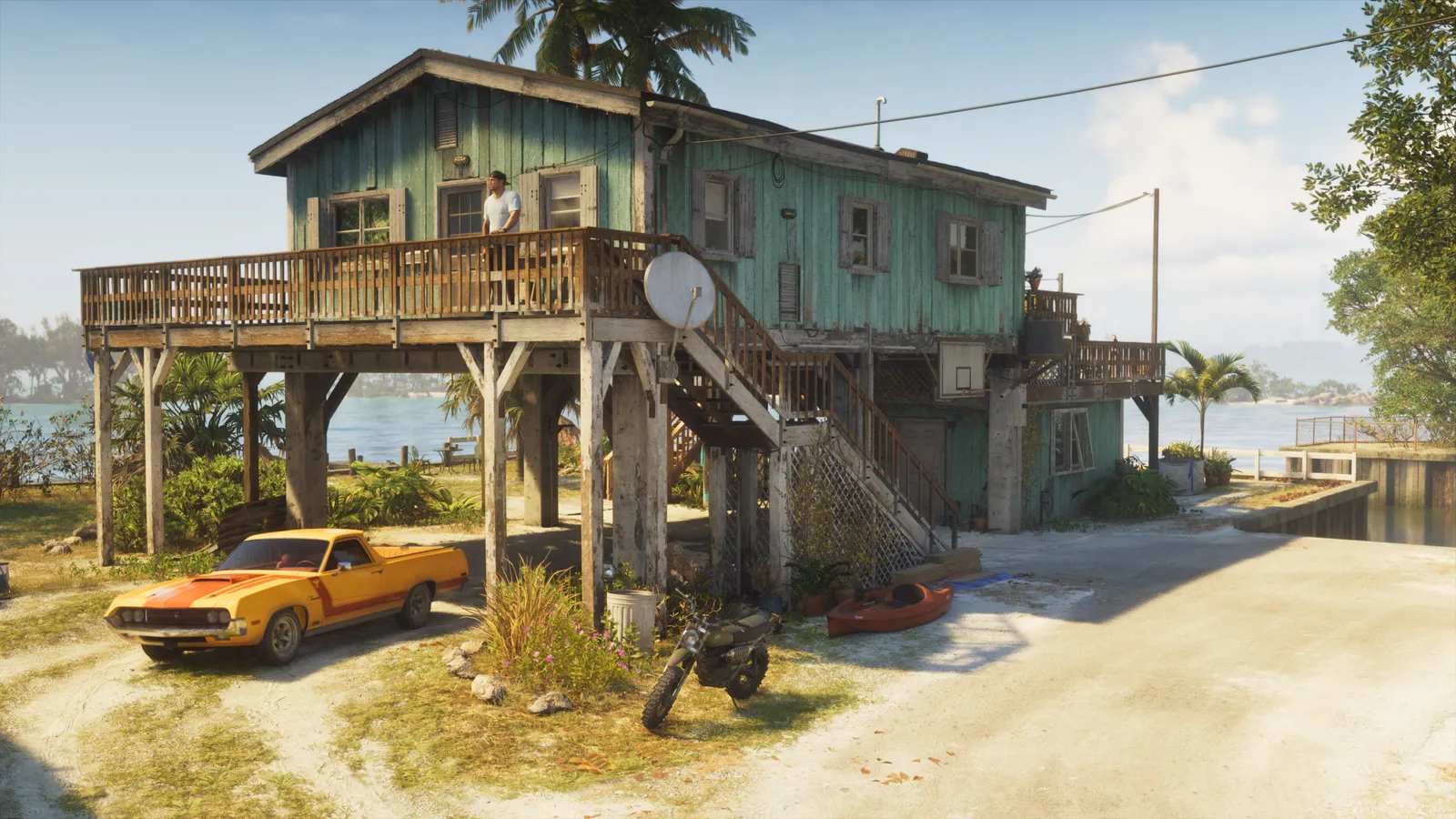 A weathered house on stilts by the water, with an orange pickup truck, a dirt bike and a kayak parked below it