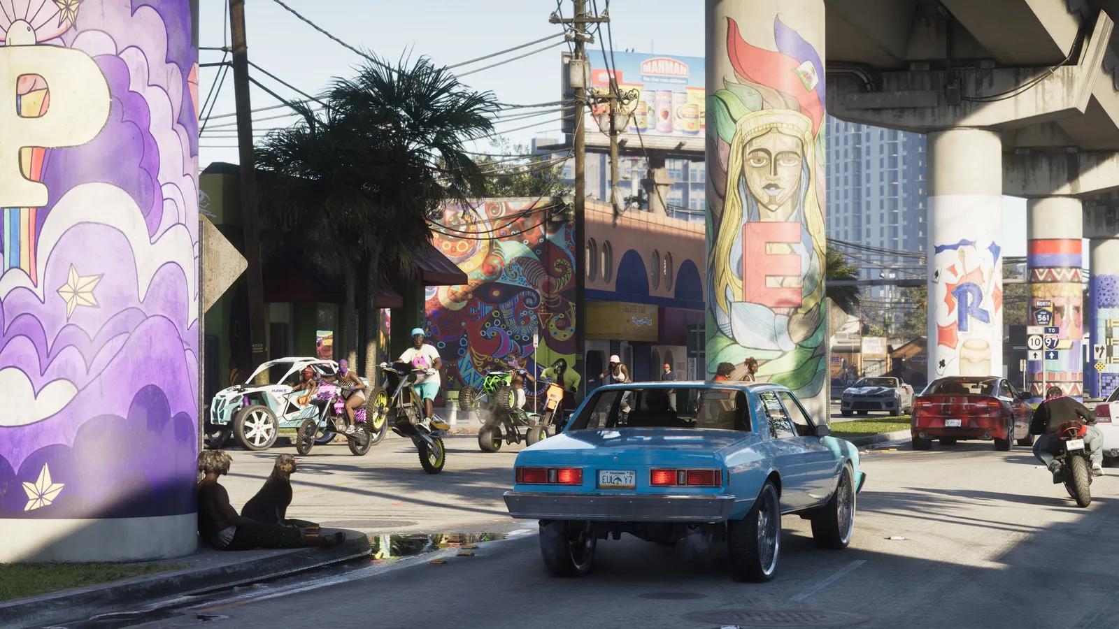 Dirt bike riders pop wheelies past a pale blue sedan on a Vice City street lined with murals beneath an overpass